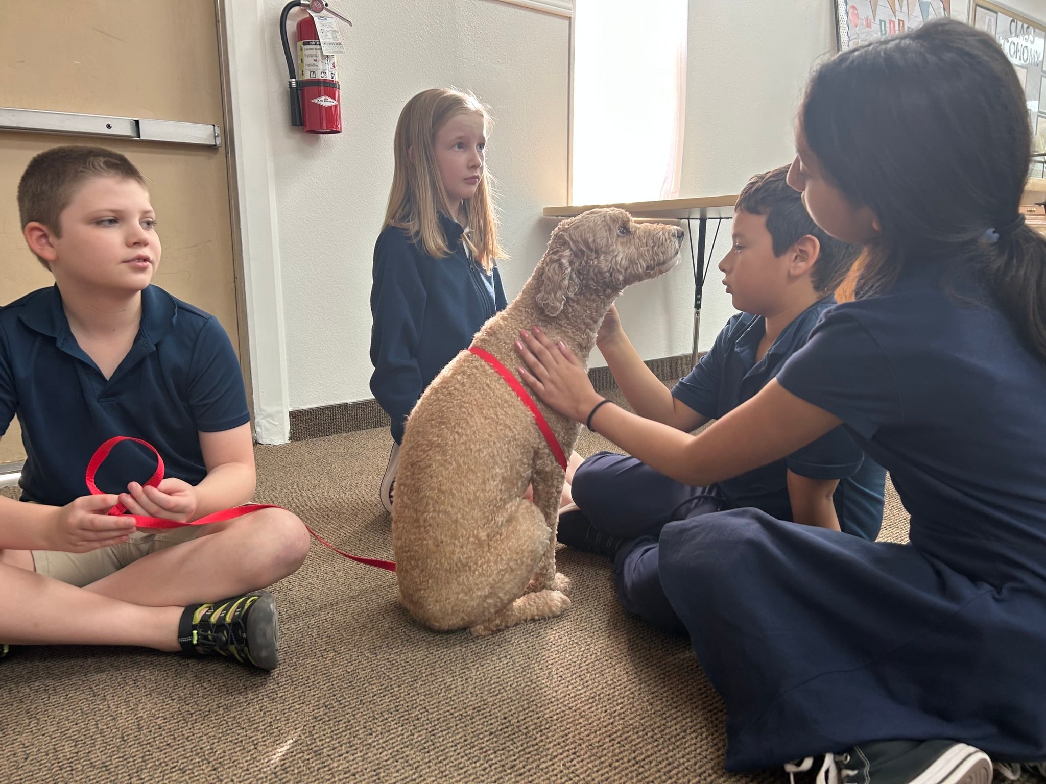 Canyon Heights students in uniform sit on the classroom floor petting a visiting dog