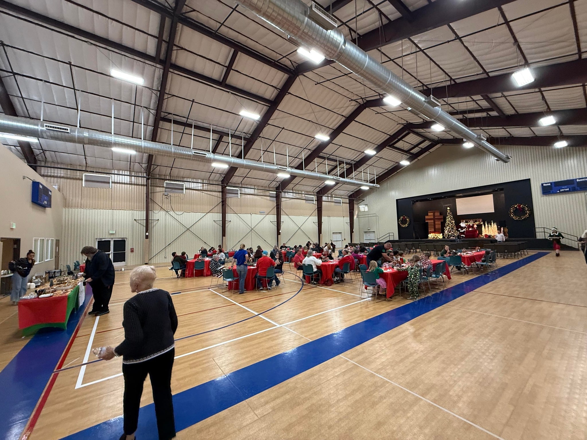 People gather at tables for a community meal in the Paloma gymnasium