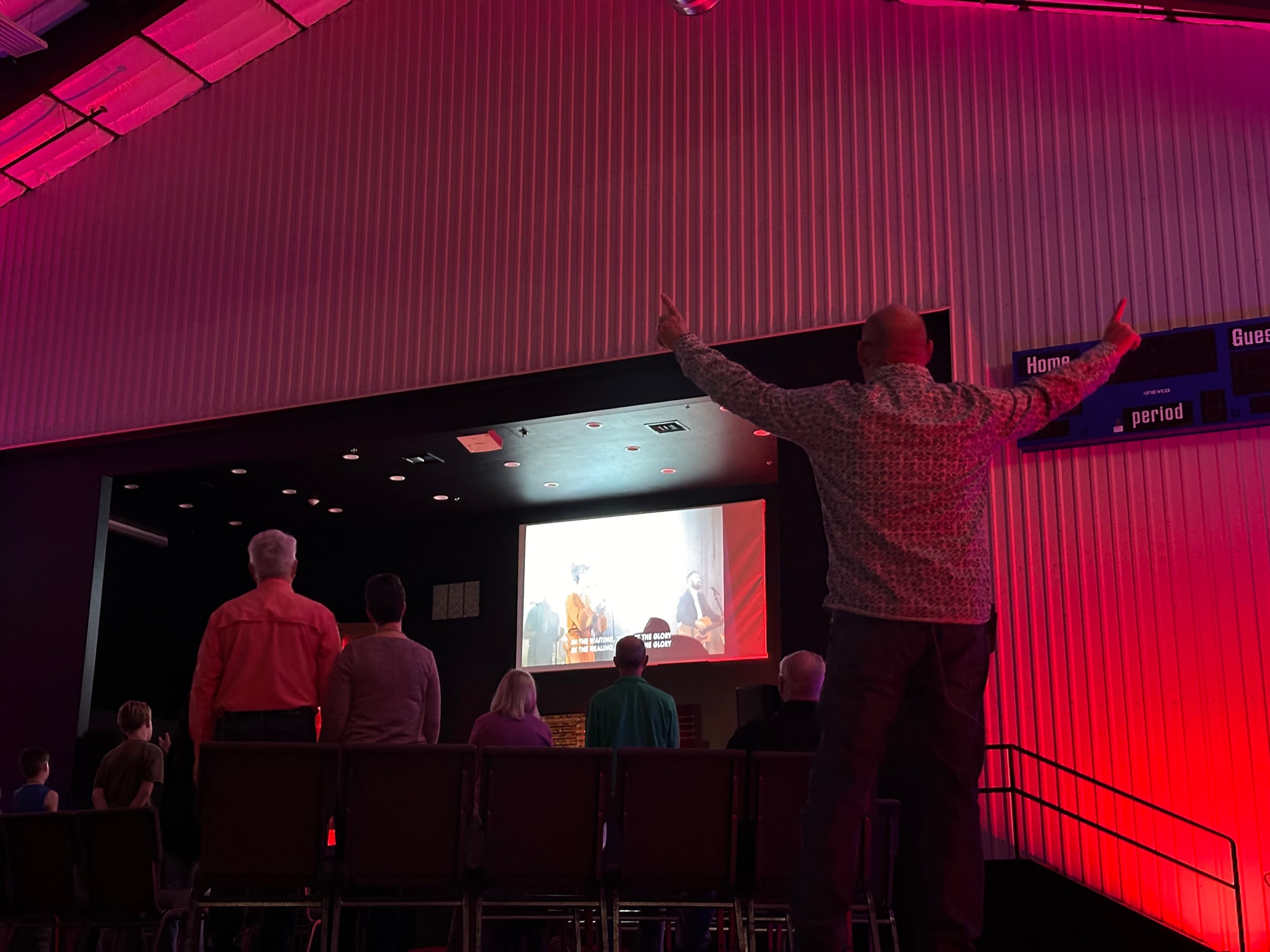 People stand in a red-lit room watching a video teaching on the screen during Experiencing Prayer