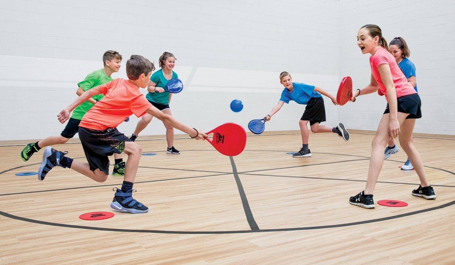 Kids with red paddles play pickleball on the indoor court at Paloma