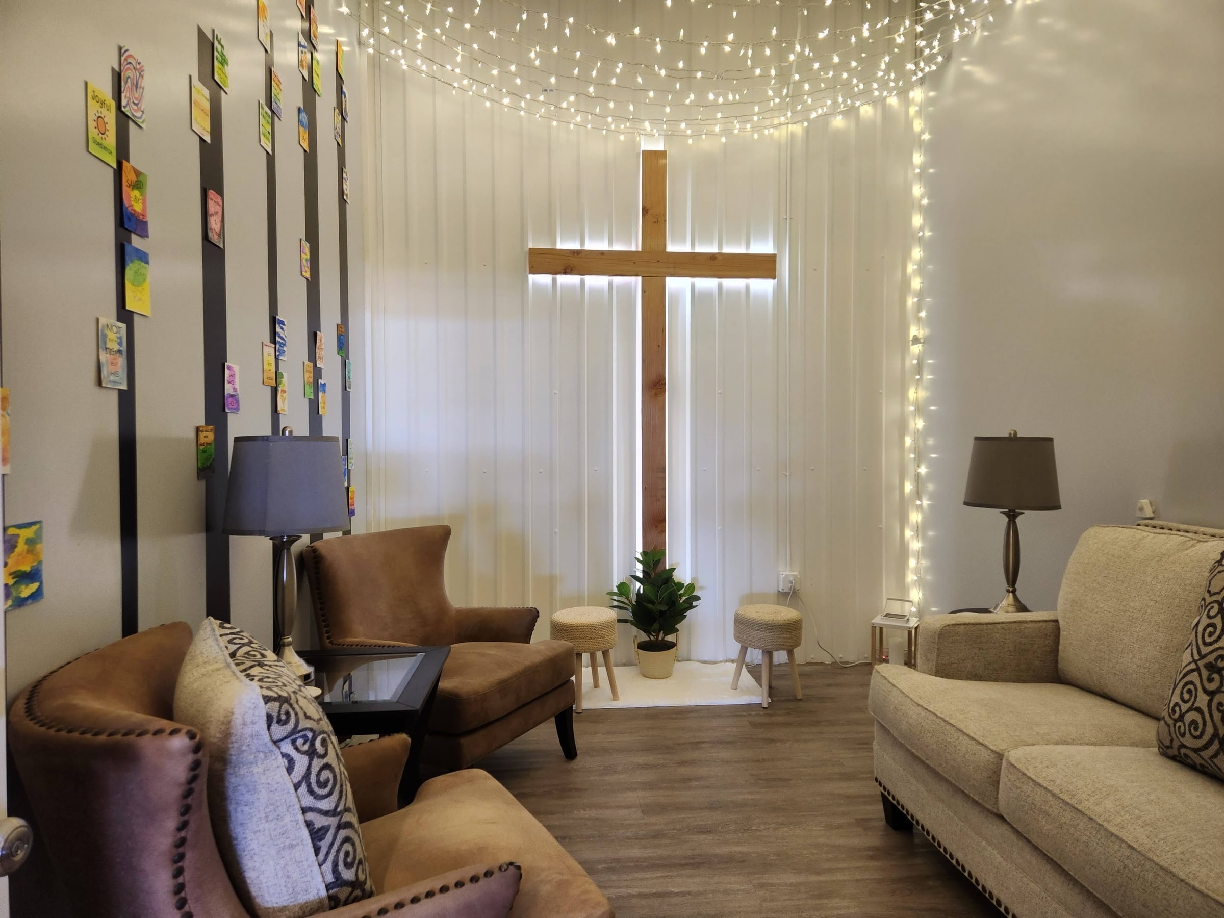 A quiet prayer room with soft chairs, string lights and a lit wooden cross