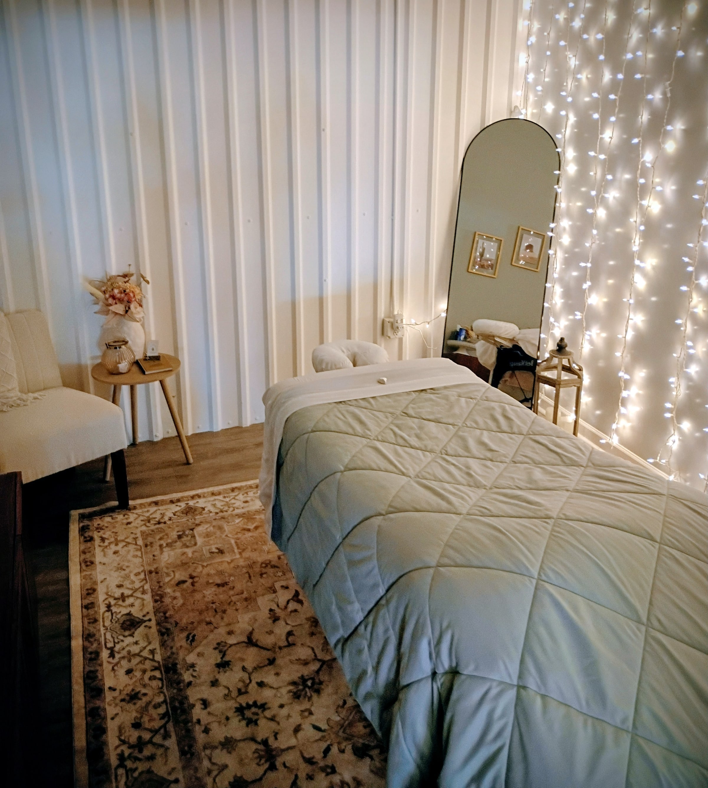 A calm massage room with a made-up table, plants and soft string lights