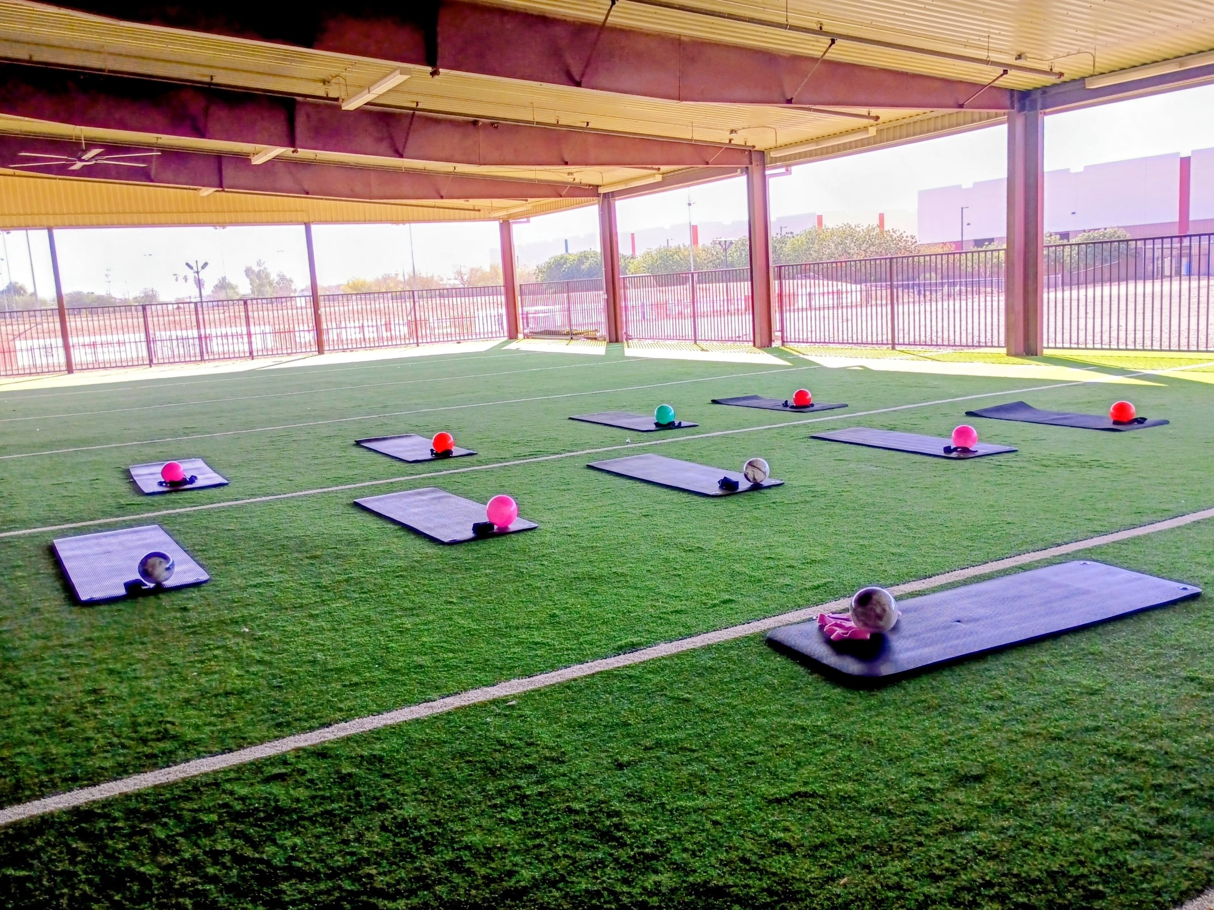 Exercise mats and weights laid out on the turf under a covered outdoor area, ready for a class