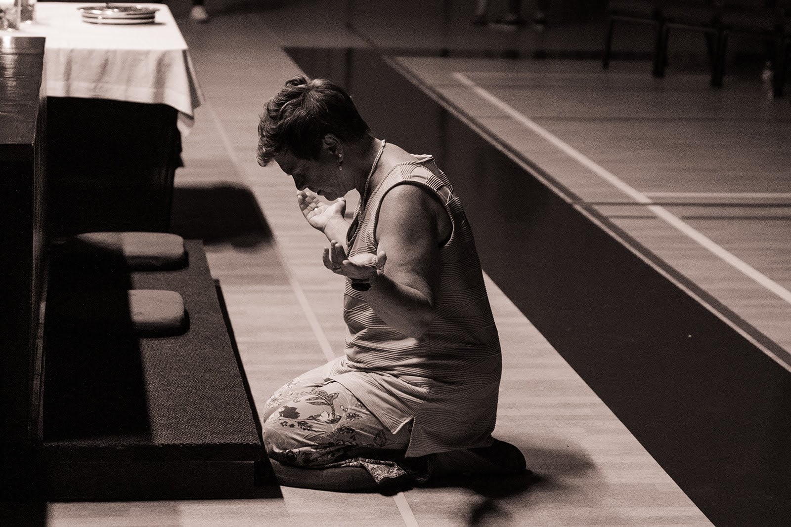 Black-and-white photo of a woman kneeling in prayer at the front of the hall