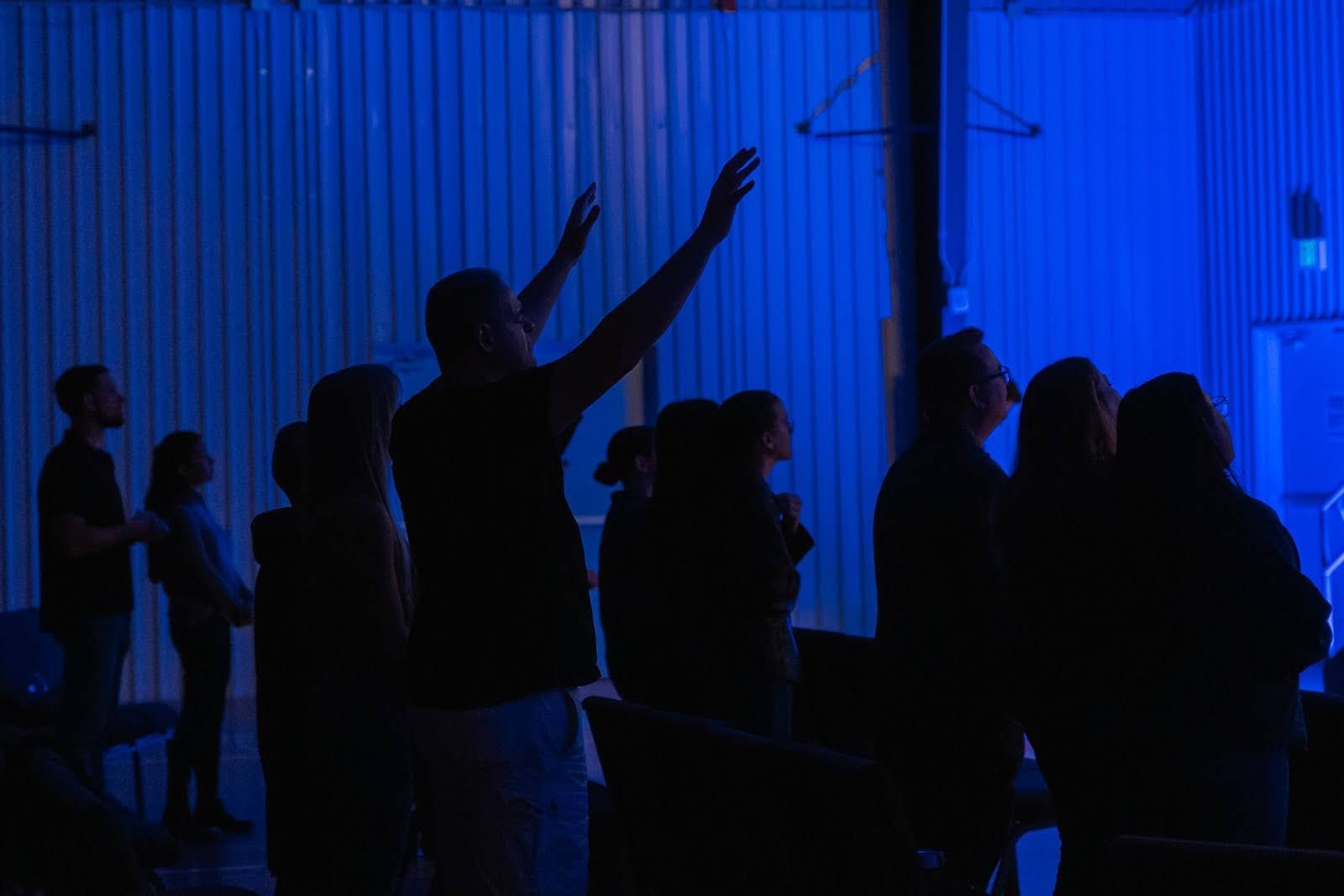 People stand and lift their hands in worship in a blue-lit hall