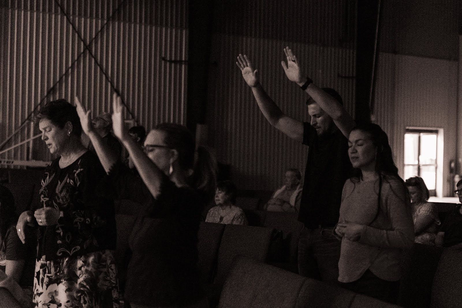 Black-and-white photo of people worshipping with raised hands in the hall