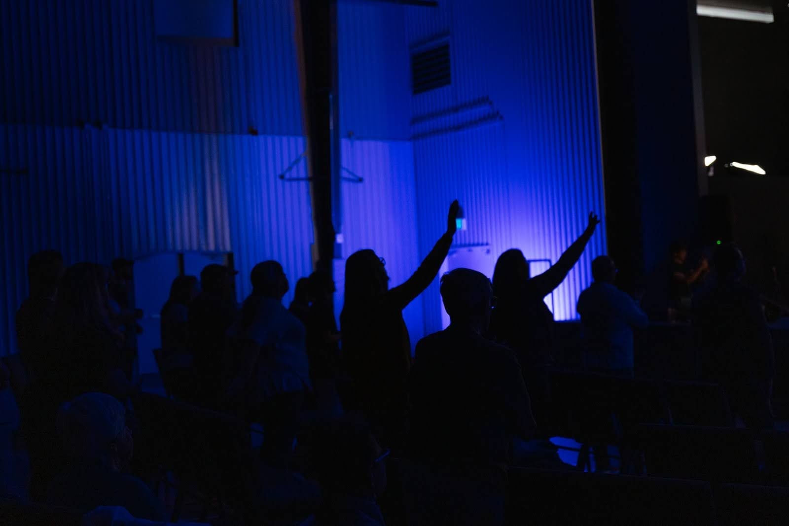Silhouettes of worshippers with raised hands in a dark, blue-lit room