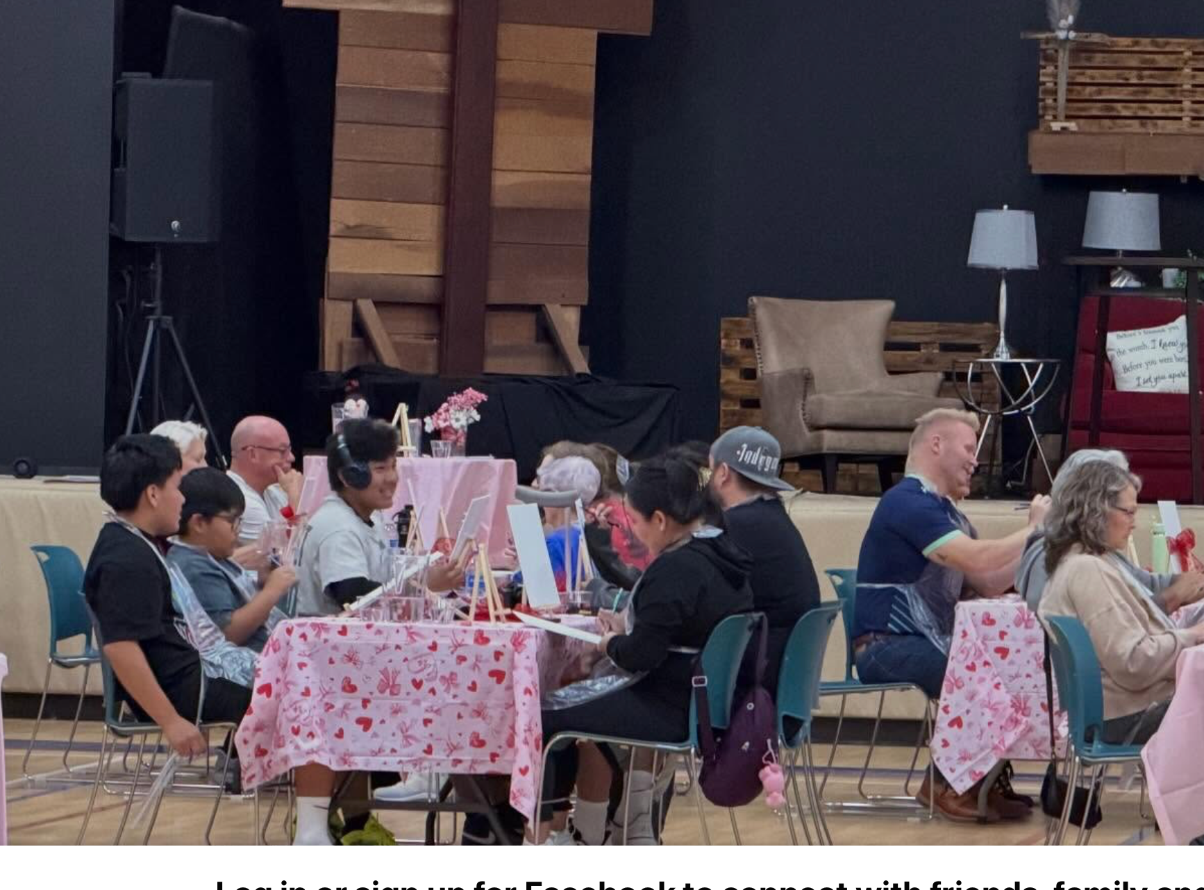 Paloma Table: people of all ages at tables with pink heart-print cloths, painting small canvases on easels in the community center hall.